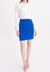 Bílá blůza s límcem ve tvaru mašle, dlouhými rukávy a detaily na manžetách, v kombinaci s sukní do kolen v jasně modré barvě a nahými lodičkami na vysokém podpatku.