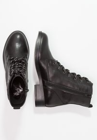 Mustat nahkaiset nilkkasaappaat kiiltävällä pinnalla, joissa on nauhakiinnitys edessä, koristeellinen sivuvetoketju ja paksu, teksturoitu pohja.