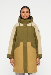 Oliwkowa i beżowa parka z kapturem, z dwoma przednimi kieszeniami, regulowanymi sznurkami i guzikami w mankietach. Posiada wzór w blokach kolorystycznych.