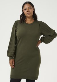 Robe en tricot verte avec des manches ballon côtelées et un col rond. Elle présente une coupe décontractée et un ourlet côtelé, offrant une texture douce.
