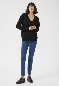 Pull noir à col en V avec des manches longues, associé à un jean bleu. Les chaussures comprennent des mocassins noirs avec des accents texturés et une semelle épaisse.
