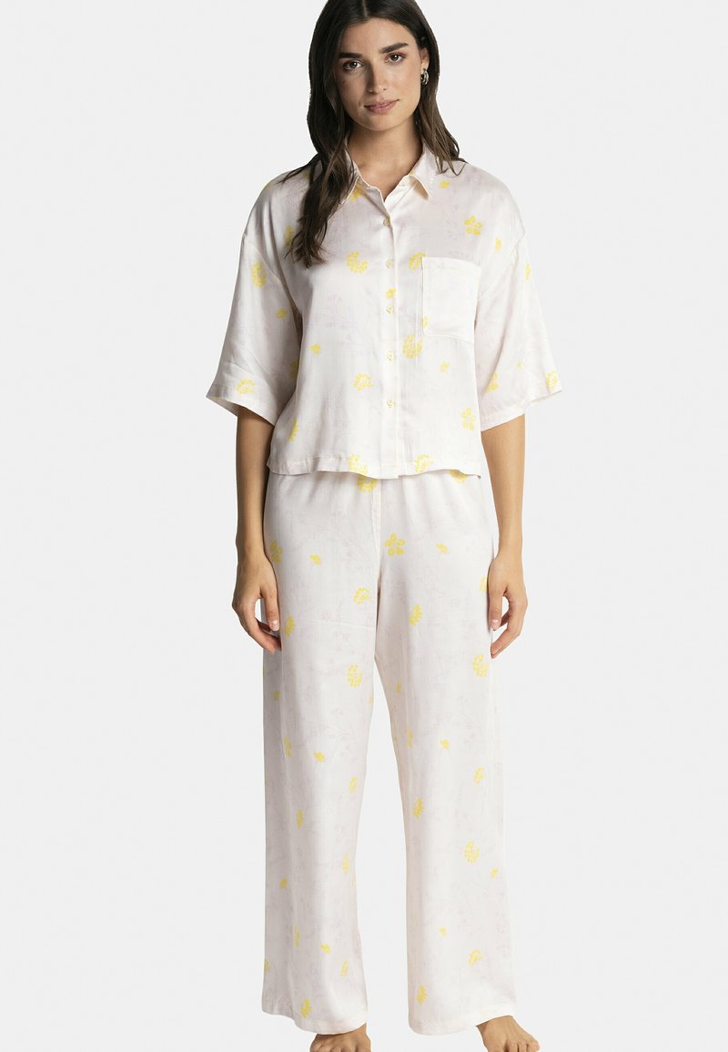 Ensemble de pyjama rose clair à manches courtes en tissu doux, arborant des motifs floraux jaunes. Le haut a une poche ; le pantalon est de style large.
