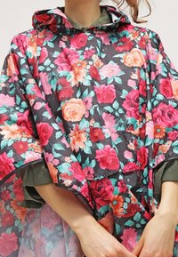 Kwiatowy płaszcz przeciwdeszczowy z czarnym tłem i dużymi różowymi, czerwonymi oraz turkusowymi kwiatami. Zawiera kaptur i szerokie, luźne rękawy.