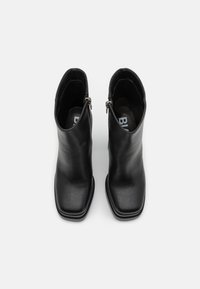 Black leather ankle boots with a square toe, smooth texture, side zippers, and a minimalistic design. Flat heel for a streamlined look.