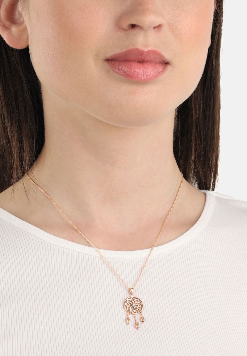 Halsband i rosguld med drömfångare-design, med intrikat cirkulär detalj och tre hängande accenter, bärs på en vit ribbad topp.