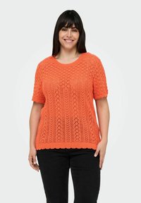 Oranje gebreide trui met korte mouwen, voorzien van een opengewerkt patroon en een golvende zoom, gecombineerd met zwarte broek.