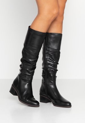 Czarne skórzane kozaki za kolano z luźnym fasonem, kwadratowym noskiem i niskim słupkowym obcasem. Wyposażone w boczny zamek błyskawiczny dla łatwego zakładania.
