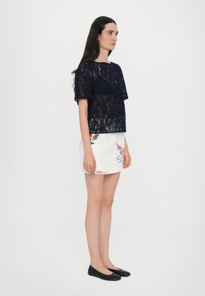 Navy lace short-sleeve top features floral patterns; paired with a white skirt embellished with colorful embroidery and black flat shoes.