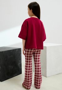 T-shirt oversize color marsala con maniche corte abbinata a pantaloni a palazzo a quadri nei toni del rosso e del beige. Tessuto morbido, vestibilità casual.