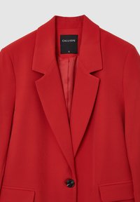 Blazer rosso realizzato in tessuto liscio, con rever a punta, chiusura con un singolo bottone nero e un design minimalista. Etichetta della taglia visibile all'interno.