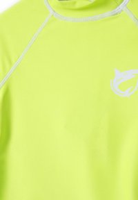 Neon žltý rash guard s vysokým golierom, plochými švami a bielym logom žraloka na prednej strane. Hladká, elastická látka.