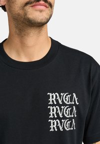 Sort kortærmet T-shirt med et tekstureret hvidt grafisk motiv på venstre bryst, der gentager "RVCA" bogstaverne, rund halsdesign.