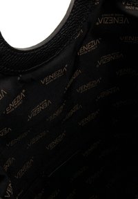 Wnętrze czarnej skórzanej torebki o gładkiej fakturze, z wzorzystą podszewką w złotym kolorze, z napisem "VENEZIA MADE IN ITALY."