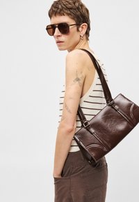 Καφέ δερμάτινη τσάντα χειρός με παραλληλόγραμμο σχήμα, που διαθέτει διπλές λαβές, υφή και διακριτές κυρτές λεπτομέρειες.