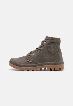 Bottines montantes en toile verte avec capuchon en caoutchouc et semelle texturée. Équipées d'œillets en métal, d'un patch logo et d'un système de laçage.
