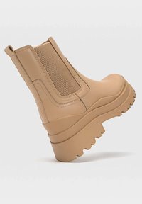 Bottines beiges à semelle compensée, avec des empiècements élastiques, en matériau synthétique lisse, accents nervurés et un motif de semelle robuste.