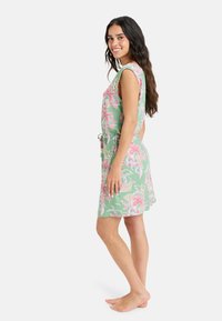 Vestido floral en verde con flores rosas y blancas. Diseño sin mangas, ajustado en la cintura con un lazo. Textura suave, hasta la rodilla.