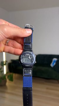 Casio digitaalikello, jossa musta muovikuori, valaistu LCD-näyttö ja kaksivärinen ranneke, jossa on teksturoitua sinistä kangasta ja sileää mustaa nahkaa.