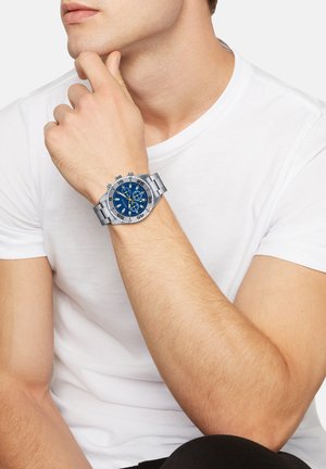 Sølv rustfrit stål ur med en blå urskive, der har sølv detaljer, chronograph funktioner og markante time markører.