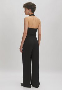 Zwarte jumpsuit met halternek, open rug en wijd uitlopende pijpen. De stof lijkt soepel met een getailleerd bovenstuk en een losse onderhelft.