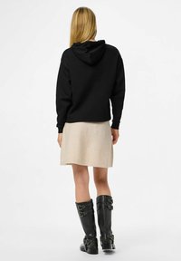 Svart huvtröja, ljusbeige kjol och knähöga svarta läderstövlar med spänne. Enkelt mönster, släta texturer.