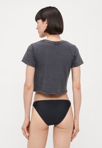 Przycięta szara koszulka z krótkimi rękawami, z surowym wykończeniem. W zestawie z czarnymi majtkami bikini z kontrastowym przeszyciem wzdłuż krawędzi.