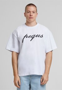 Fehér, rövid ujjú póló, kerek nyakkivágással, amelyen nagy fekete írásos logó "pequs" látható a mellkason. Puha pamut anyag, laza szabás.