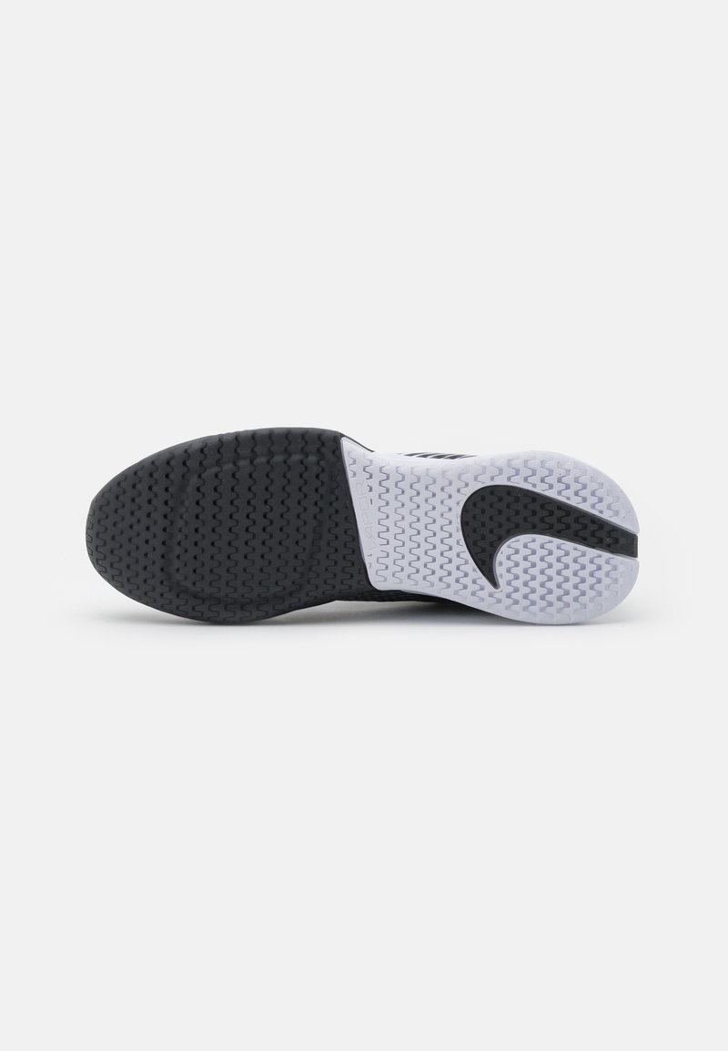 Semelle de chaussure de sport noir et blanc avec une surface en caoutchouc texturé, un motif de bandes distinct, et un logo reconnaissable en forme courbée.