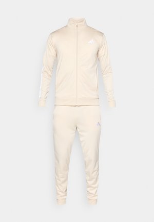 Beiger Trainingsanzug aus glattem Stoff, bestehend aus einer Jacke mit Reißverschluss und hohem Kragen sowie passenden, schmal zulaufenden Hosen, beide mit reflektierenden Details.