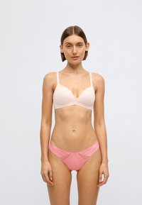 Gaiši bēšs krūšturis ar dziļu izgriezumu un plānām siksnām, kombinēts ar rozā biksītēm ar sieta akcentiem un gludu apdari.