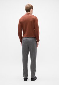 Brun langærmet skjorte og grå bukser. Skjorten har en krave og struktureret stof. Bukserne har en skræddersyet pasform med subtile design detaljer.