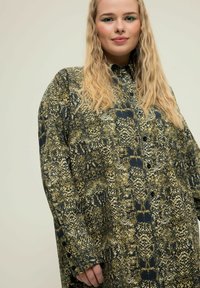 Camicia verde e nera a fantasia con una vestibilità ampia, caratterizzata da un design con bottoni e maniche lunghe. Il tessuto ha una texture liscia.