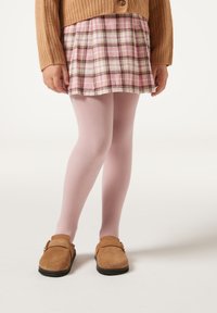 Brązowy dzianinowy kardigan, różowa spódnica w kratkę, jasnoróżowe rajstopy i brązowe buty wsuwane z czarnymi podeszwami. Skoncentrowano się na wzorach i teksturach tkanin.