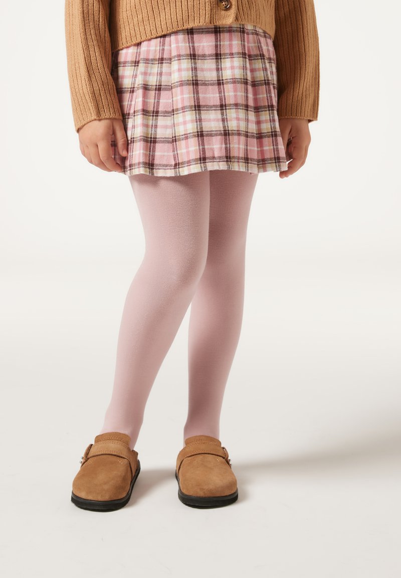 Brązowy dzianinowy kardigan, różowa spódnica w kratkę, jasnoróżowe rajstopy i brązowe buty wsuwane z czarnymi podeszwami. Skoncentrowano się na wzorach i teksturach tkanin.