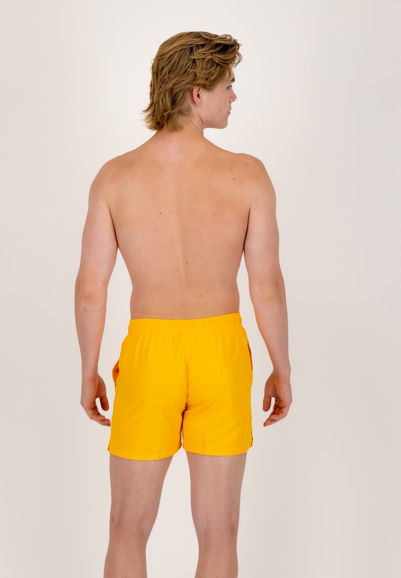 Żółte kąpielówki wykonane z lekkiego materiału, z elastycznym pasem i bocznymi kieszeniami, pokazane z tyłu.