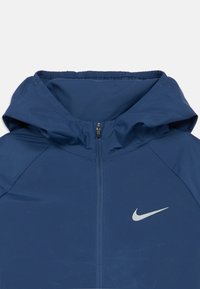 Blaue Kapuzenjacke aus leichtem Material, mit einem Frontreißverschluss und einem kleinen weißen Nike-Logo auf der linken Brust.