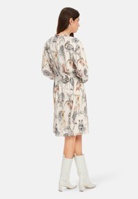 Leichtes, cremefarbenes Kleid mit Tiermuster, langen Ärmeln, tailliertem Schnitt und knielangem Saum. Kombiniert mit weißen, knielangen Stiefeln mit Absatz.