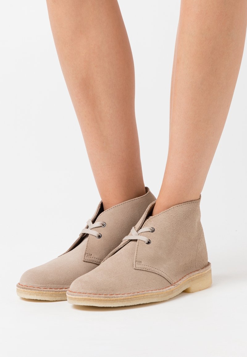 Stivaletti alla caviglia in suede beige con punta arrotondata, design con lacci a due fori e suole in gomma naturale. Tessitura liscia con cuciture minime.