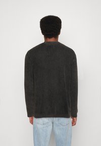 Dunkelgrauer gestrickter Pullover mit gerippter Textur, rundem Halsausschnitt und langen Ärmeln, kombiniert mit hellblauen Jeans.