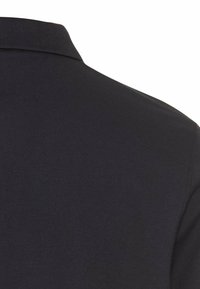 Gros plan du tissu d'un polo bleu marine foncé montrant le col côtelé et la couture d'épaule.
