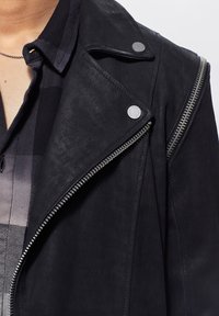 Černá kožená motorkářská bunda se stříbrnými kovovými doplňky, diagonálním zipem, zapínacím límcem a strukturovaným povrchem.