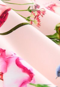 Tissu avec un fond rose clair orné de motifs floraux vibrants de roses et de œillets, accompagné d'un détail d'oiseau bleu.