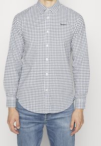 Overhemd met knopen in wit en marineblauw geruit patroon, katoenen materiaal, lange mouwen, afgeronde zoom, met logodetail op de borst.
