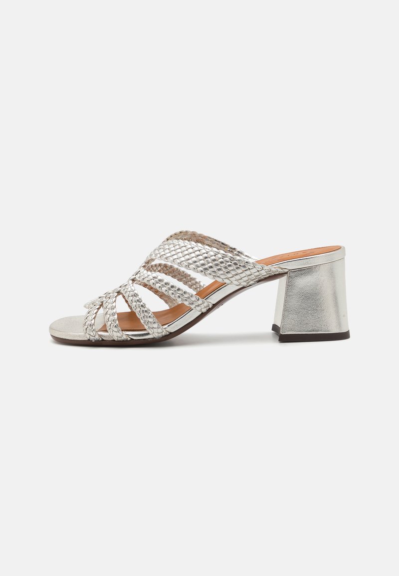 Mule aperte in argento con punta aperta, dotate di un design intrecciato, di una parte anteriore piatta e di un tacco a blocco metallico spesso. Texture liscia con accenti a contrasto.