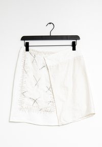 Bílá sukně s jedinečným překládaným designem a stříbrným prošíváním. Obsahuje abstraktní vzory, zakřivení spodního okraje a zavěšovací smyčku pro vystavení.