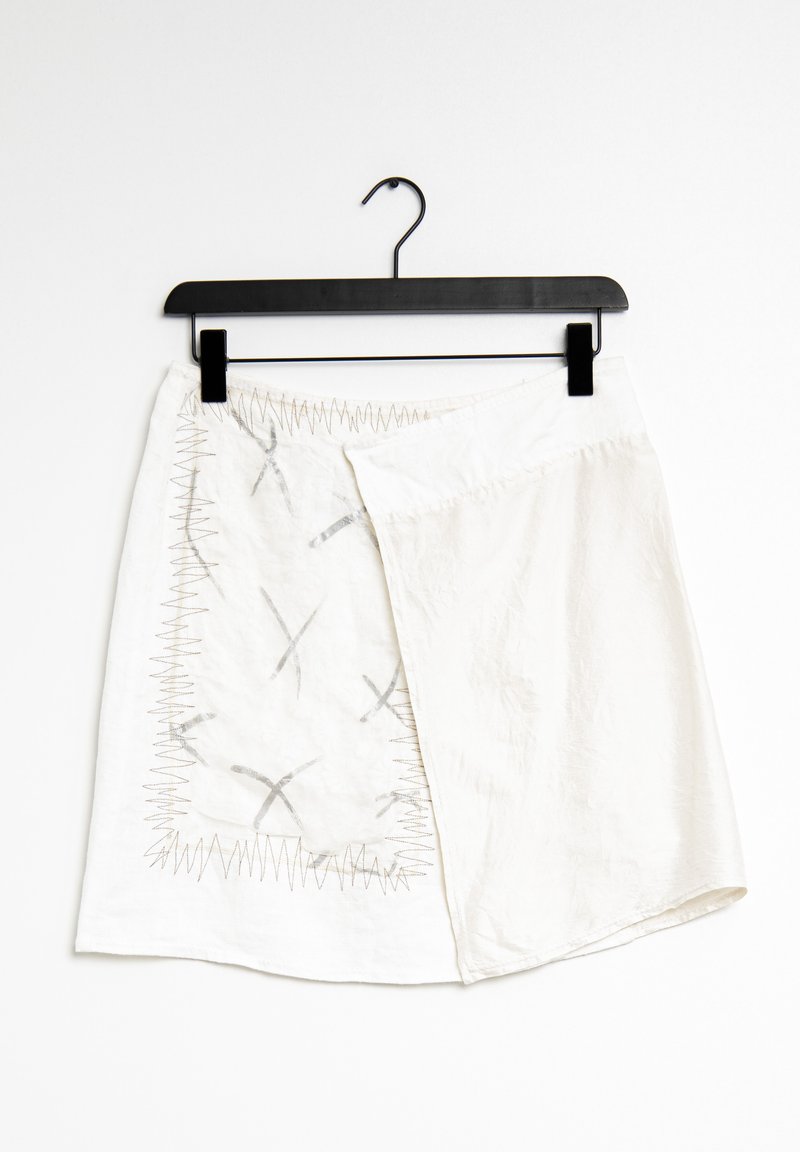 Bílá sukně s jedinečným překládaným designem a stříbrným prošíváním. Obsahuje abstraktní vzory, zakřivení spodního okraje a zavěšovací smyčku pro vystavení.