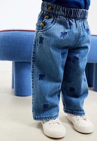 Traperice s elastičnim pojasom, s tri smeđa gumba i uzorkom tamnoplavih medvjedića. Uparene s bijelim tenisicama.