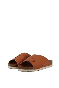 Brown leather slide sandals with wide overlapping straps, cork footbed, and a textured rubber sole. Features a neutral color palette.