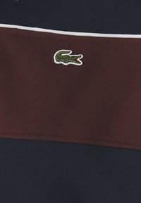 Polo tričko s farebným blokovaním v marhuľových a námorníckych častiach, vyrobené zo hladkej bavlny, ozdobené zeleným logom krokodíla.