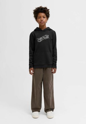 Svart hoodie med logotyp på framsidan, känguruficka och ribbstickade ärmslut, i kombination med löst sittande bruna kordflortbyxor och vita sneakers.